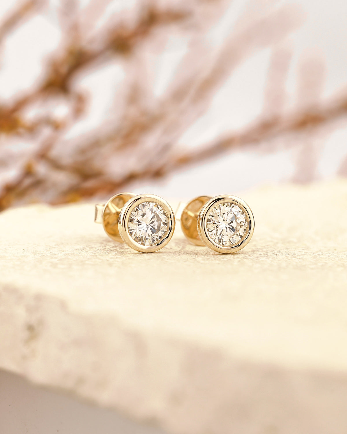 Gold bezel-set diamond stud earrings on stone
